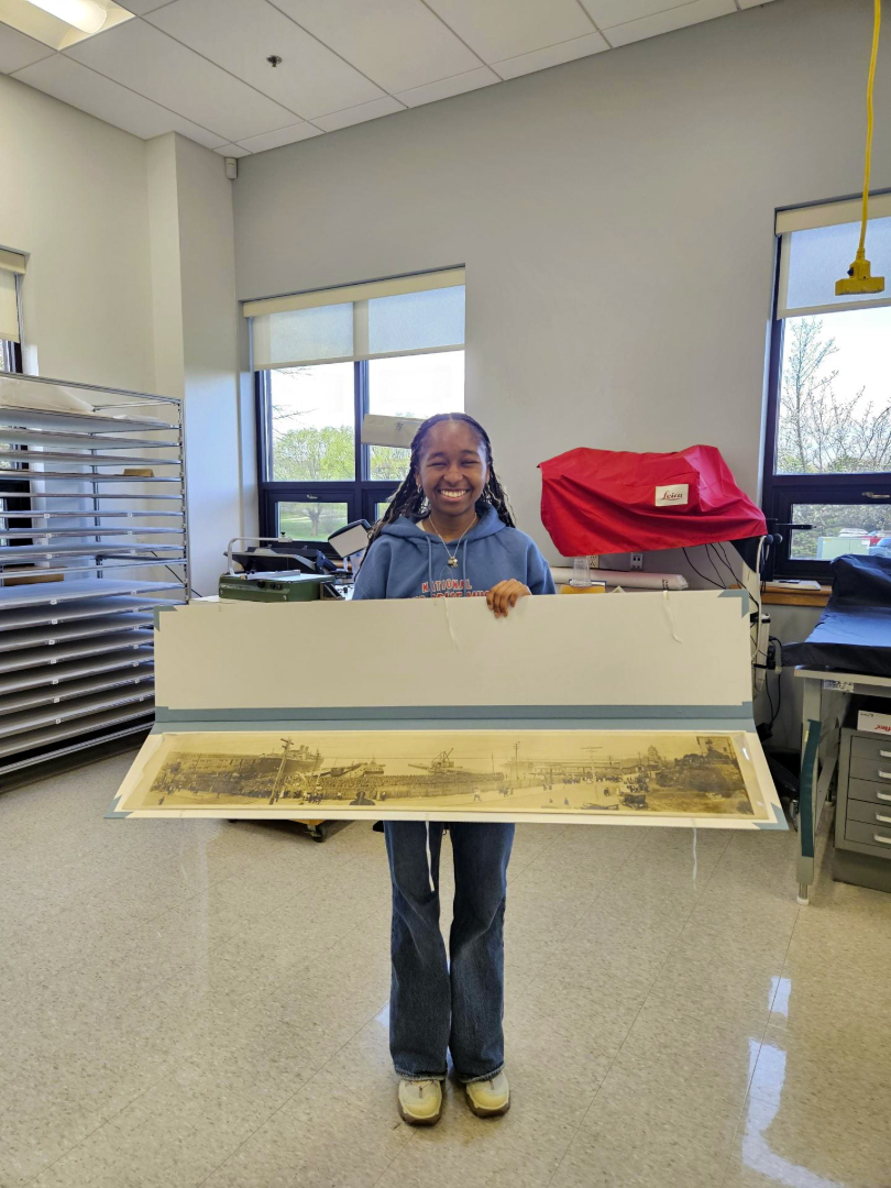 a conservator in a lab showing a large format panoramic photograph.